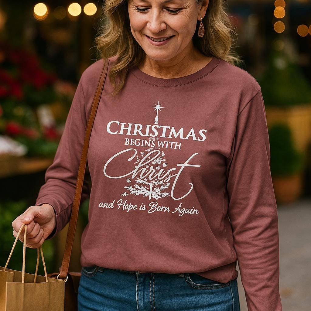 Woman wearing a maroon sweatshirt with a Christmas message, standing in a festive setting.
