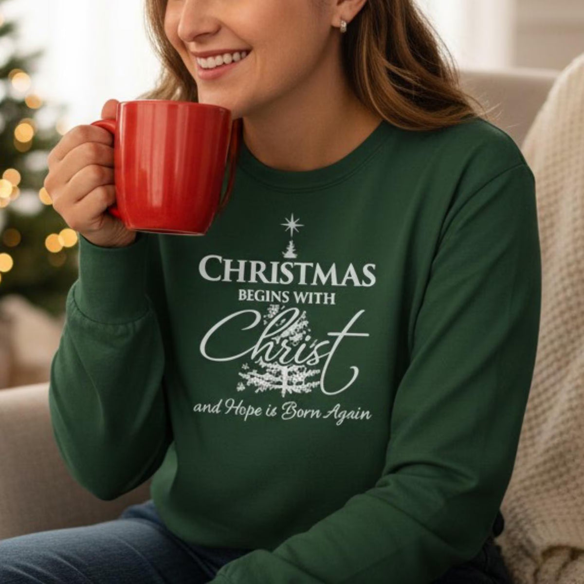Person wearing a green sweatshirt with a Christmas message, holding a red mug.