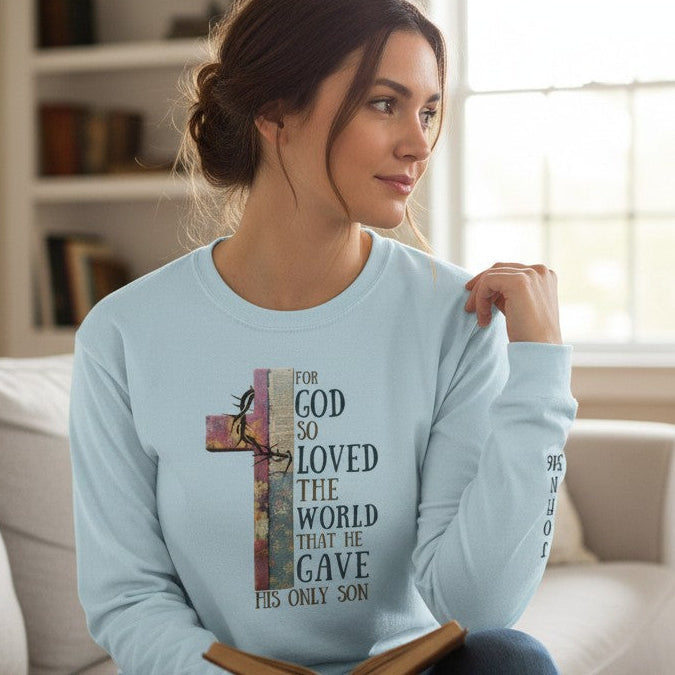 Woman sitting on a couch holding a book in a living room wearing a light blue sweatshirt with text and graphics.