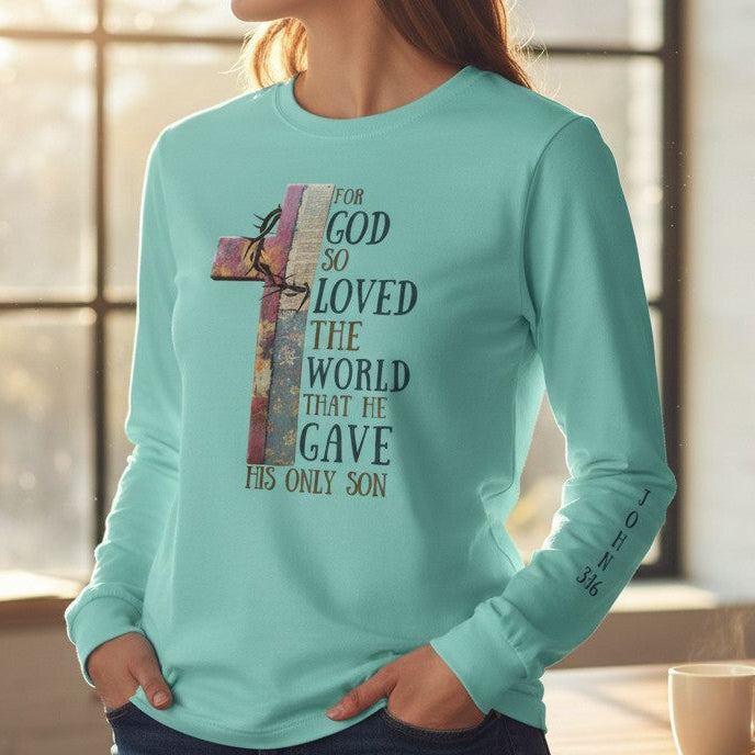 Person wearing a light blue long-sleeve shirt with a cross and text design, standing in a room with a table and books.