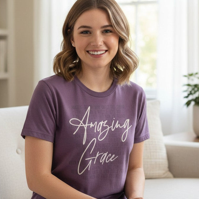 Woman wearing a purple 'Amazing Grace' t-shirt sitting on a couch in a bright living room.