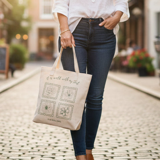 Woman walking down a street holding a tote bag with a logo, wearing a white shirt and blue jeans.