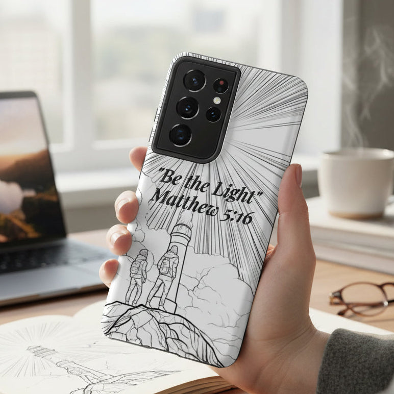 Person holding a phone with a 'Be the Light' Matthew 5:16 phone case in a home office setting.