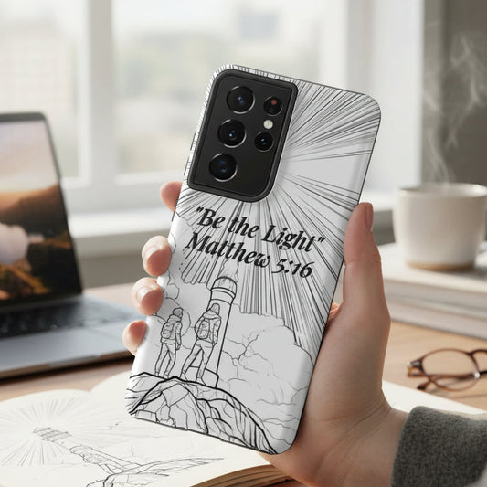 Person holding a phone with a 'Be the Light' Matthew 5:16 phone case in a home office setting.