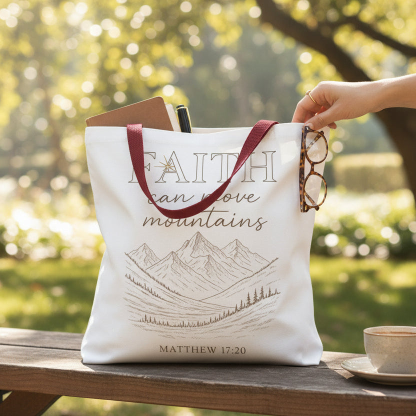 Tote bag with 'Faith can move mountains' quote on a wooden bench outdoors.