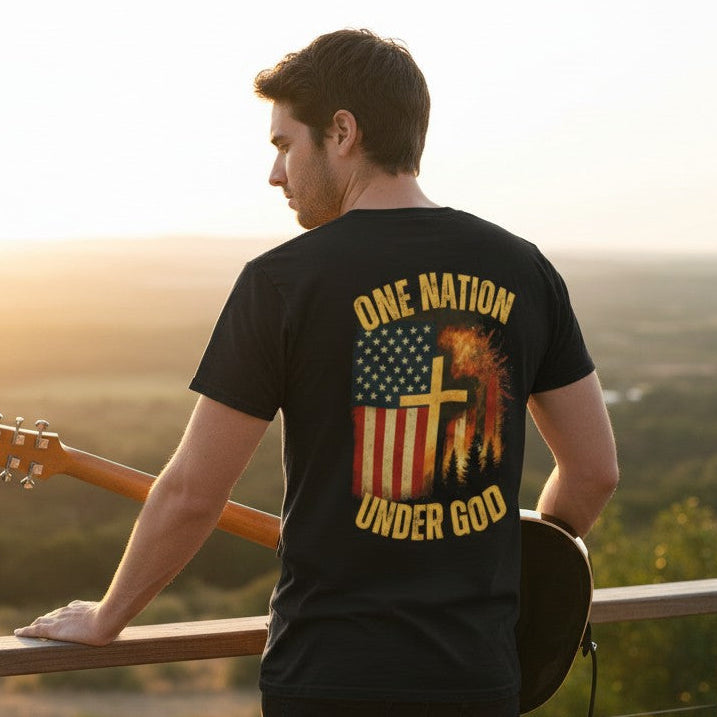 Man holding a guitar with 'One Nation Under God' shirt at sunset