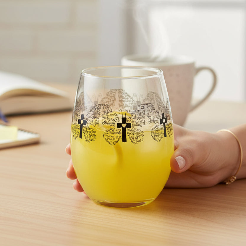Hand holding a glass of yellow liquid on a wooden table with a book and mug in the background.