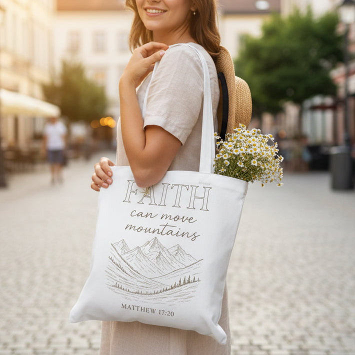 Woman holding a tote bag with 'Faith can move mountains' quote in an urban setting