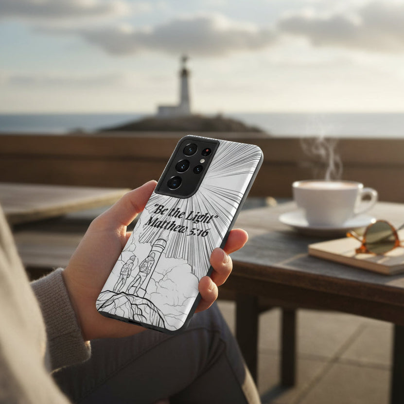 Person holding a phone with a 'Be the Light' design outdoors