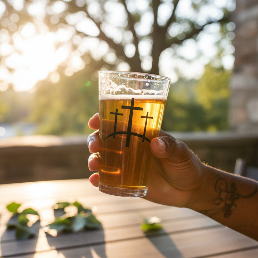 Hand holding a glass of beer with a sunset or sunrise in the background