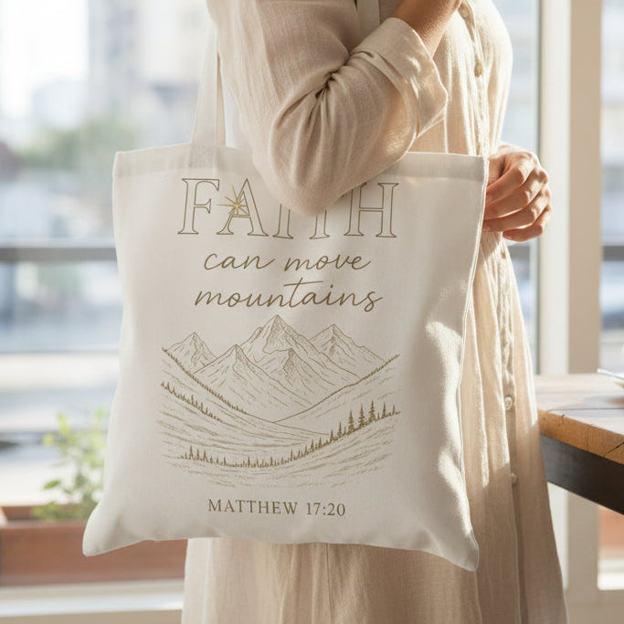Person holding a tote bag with 'Faith can move mountains' quote in a bright room.