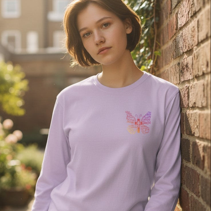 Woman wearing a light purple long-sleeve shirt with a colorful design, standing against a brick wall.
